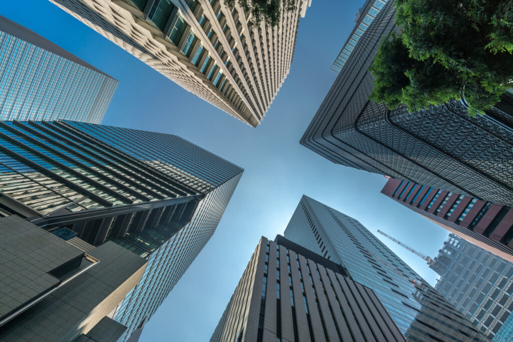 Immagine dall basso di grattacieli moderni con vetrate riflettenti e un cielo blu sopra, catturando l'architettura urbana contemporanea